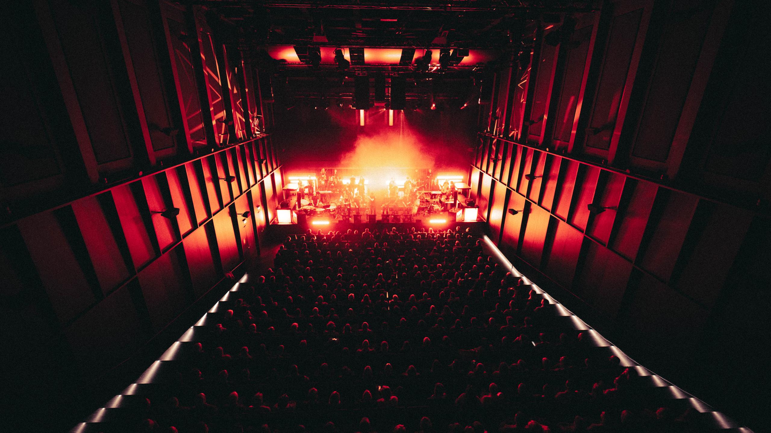 Blick aus dem oberen Rang auf das Konzert „Eine Technosinfonie“ im Bergson Kunstkraftwerk: Bühne in rotes Licht getaucht, volles Publikum im Elektra Tonquartier.