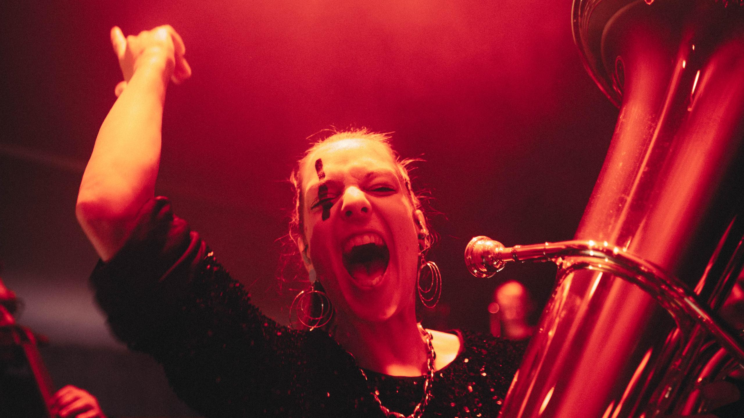 Tuba-Spielerin der Jazzrausch Bigband in euphorischer Pose während „Eine Technosinfonie“ im Bergson Kunstkraftwerk – Bühnenlicht in intensivem Rot.