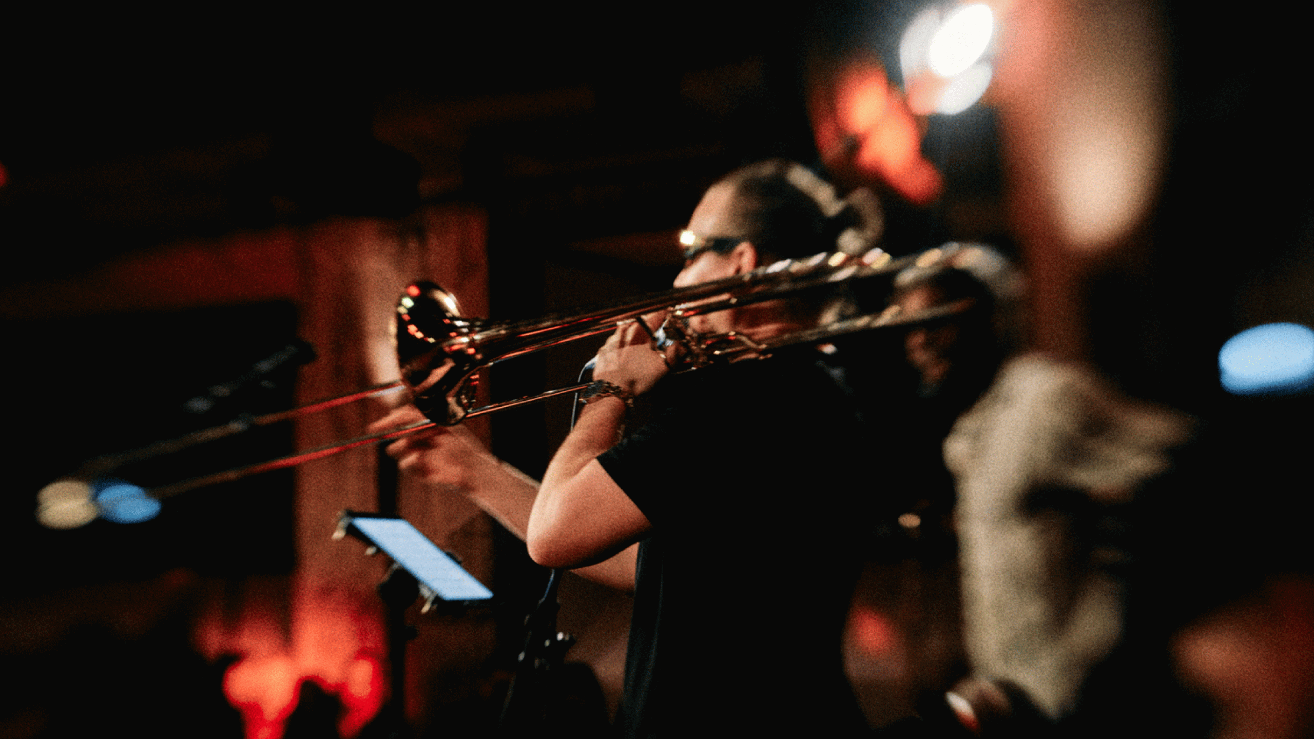 Posaunist spielt live auf der Bühne bei Jazzkonzert mit warmer roter Beleuchtung und unscharfem Publikum im Hintergrund