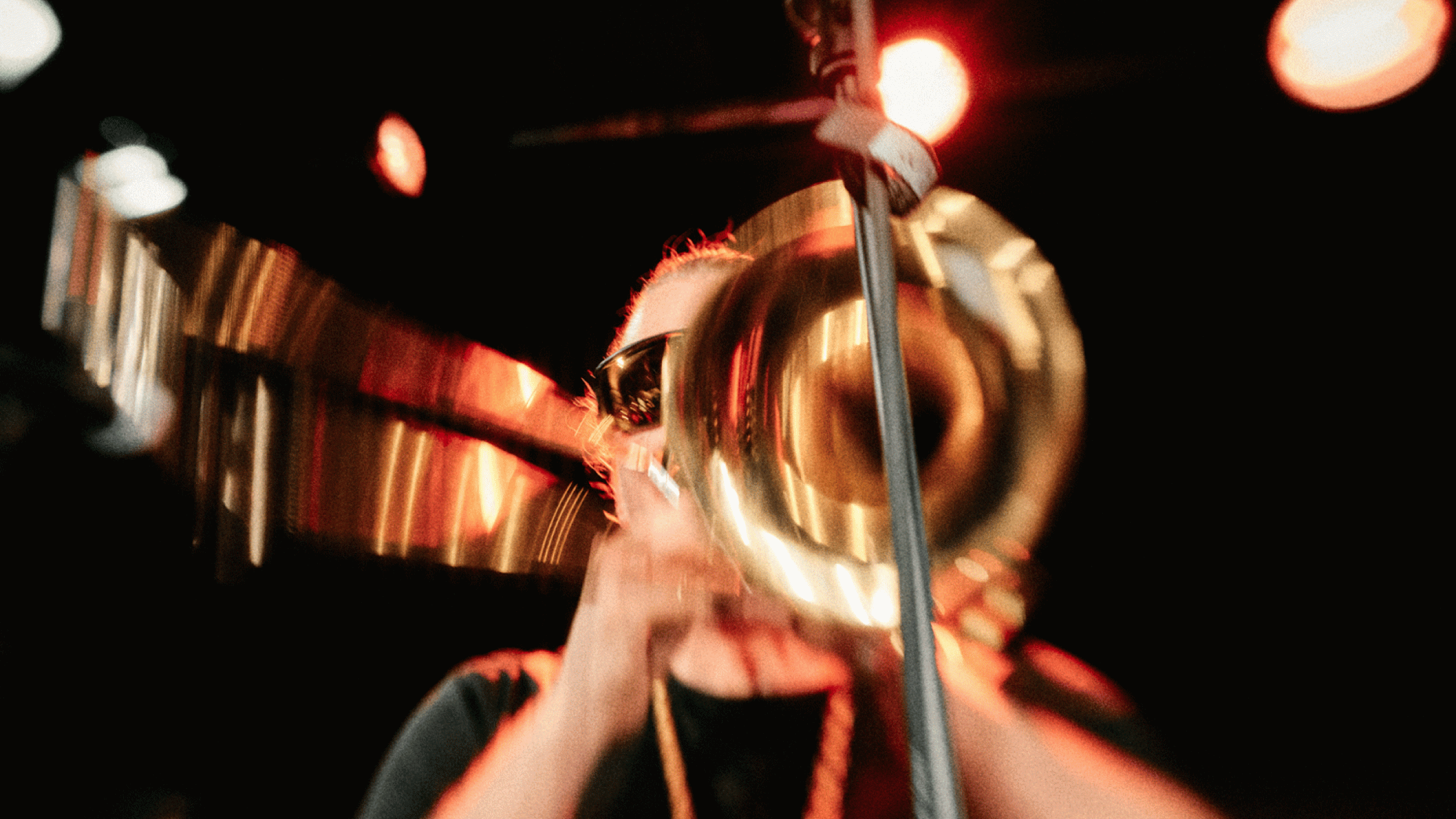 Posaunist spielt Trombone mit Bewegungsunschärfe bei energiegeladenem Live-Konzert unter roter Bühnenbeleuchtung